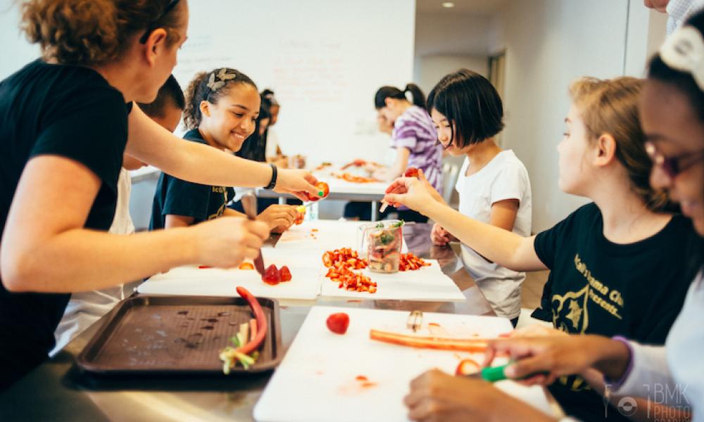 A group of children and a teacher slicing vegetables. Photo courtesy of the Free Library of Philadelphia's Culinary Literacy Center.